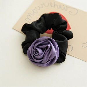 Detailed view of a black elastic scrunchie featuring a purple satin rose flower