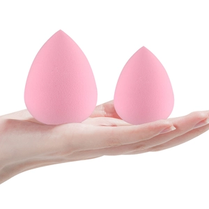 Size comparison of two pink teardrop makeup sponges held in hand on white background