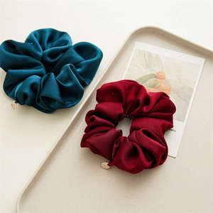 Close-up of premium navy and burgundy satin scrunchies with metal charms on a tray
