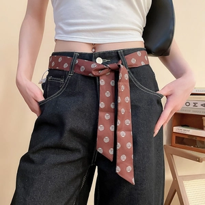 Dettaglio di una cintura a foulard in seta a quadri marroni su jeans scuri larghi
