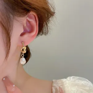 Detailed view of elegant baroque pearl earrings with golden knot studs on a model