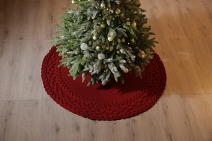 Close-up of red knitted Christmas tree skirt with diamond pattern on wood floor