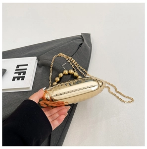 Close-up of golden hard-shell evening bag with pearl handle and detachable metal chain