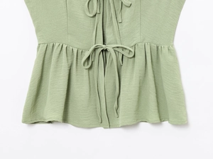 Detail of light green top showing textured fabric with drawstring ties and ruffled hemline