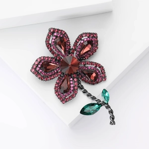 Détail de broche fleur aux strass rouges et feuilles de gemmes vertes sur tige noire