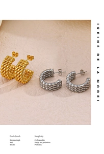 Detail showing gold and silver twisted rope C-hoop earrings on beige texture surface