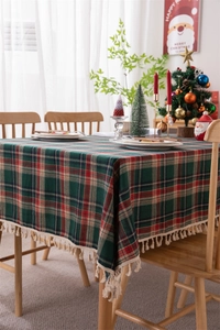Detail of red and green plaid Christmas tablecloth with beige tassels on a wooden dining table