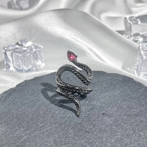 Detail of snake ring with red gemstone eye on dark grey stone and white silk background