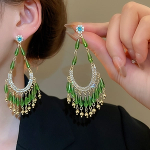 Détail de boucles d'oreilles de luxe à pompons émeraude avec cristaux et cadre doré