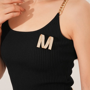 Detailed view of luxury gold M letter brooch with sparkling rhinestones on black fabric