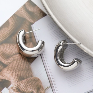 Polished silver C-shaped geometric hoop earrings displayed on a fashion magazine
