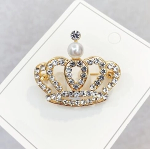 Detailed macro view of gold crown brooch with sparkling rhinestones and white pearl inlay