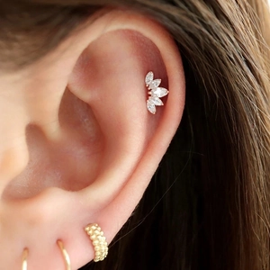 Detail showing a silver crown cartilage stud with marquise stones and gold hoop earrings