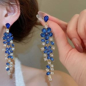 Close-up of elegant gold tassel earrings with blue and clear crystal floral accents