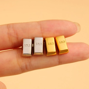 Close-up of square 18K gold and silver stud earrings featuring engraved GOLD text