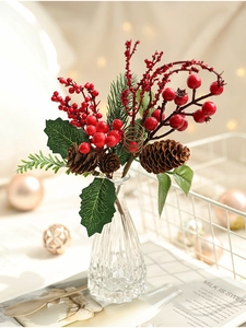 Christmas pine cone and red berry picks displayed in a glass vase with warm ambient lighting