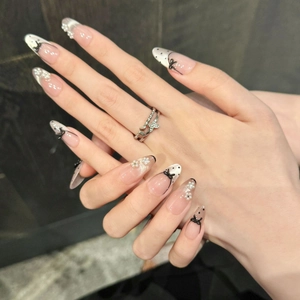 Detail of almond-shaped press-on nails with bow designs, pearls, and black polka dots
