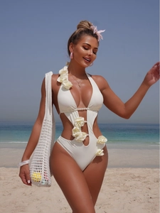 White 3D flower cutout one-piece swimsuit with pearl details on a sunny beach