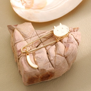 Close-up of a cute gold-plated cat safety pin brooch with white enamel on a natural stone
