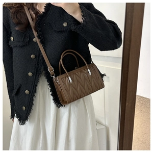 Brown pleated handbag with wave texture shown on shoulder of a model in black jacket