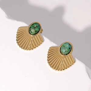 Macro view of golden fan-shaped earrings with green stone inlays on white textured stone