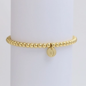 Close-up of golden beaded stretch bracelet with letter O charm on white pedestal