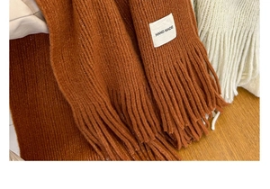 Detail of knitted scarf texture and tassel with hand made label on wooden surface