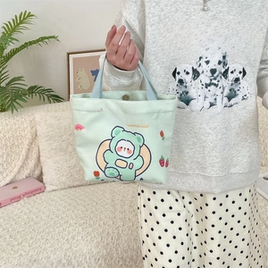 Detail of light green canvas tote bag featuring a cute cartoon bear and top handle