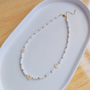 Close-up of handmade daisy beaded choker with white heishi beads and gold lobster clasp
