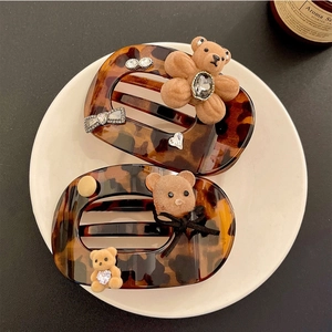 Brown tortoiseshell claw clips with flocked bear and rhinestones in a white ceramic dish