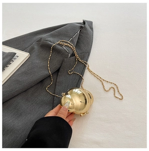 Close-up of a mini golden spherical metal shell bag with a delicate link chain strap
