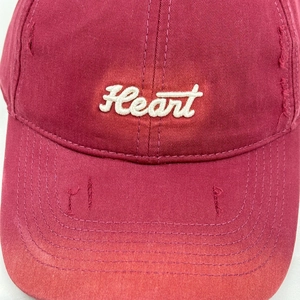 Detailed view of embroidery and distressed holes on burgundy cotton baseball cap