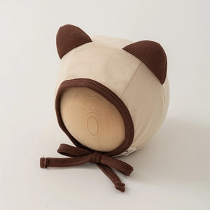 Close-up of beige knit newborn hat featuring cute brown bear ears and earflap ties