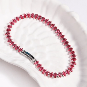 Macro shot of silver tennis bracelet featuring marquise-cut red zircon stones on a white tray