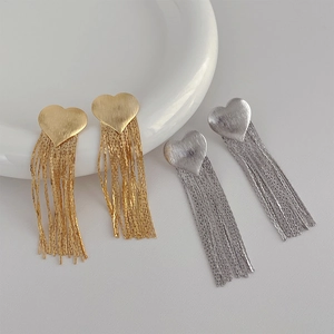 Close-up of gold and silver heart tassel earrings with brushed matte metal texture