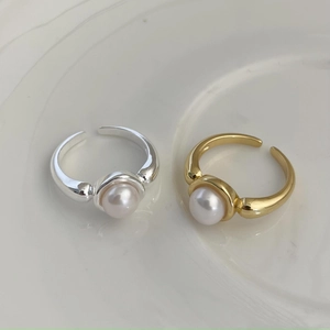 Macro view of adjustable silver and gold pearl rings on white ceramic surface