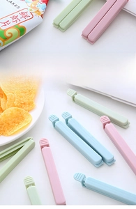 Close-up of three pastel-colored long food sealing clips on snack packaging bags