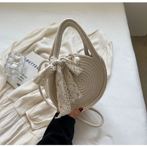 Detail of round cream woven handbag featuring delicate lace bow and pearl decoration