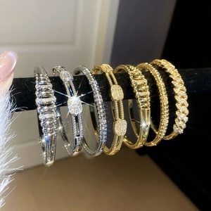 Macro view of gold and silver wave bangles with pave-set zircons on black display