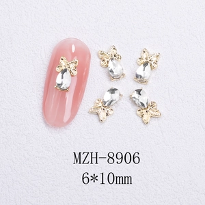 Macro shot of 6x10mm gold alloy bow and teardrop crystal nail art gems on white sand