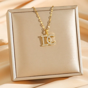 Collier lettre DC doré avec zircons micro-pave sur une boîte à bijoux en soie