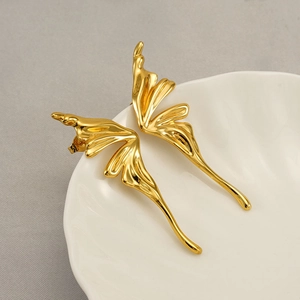 Macro shot of liquid metal gold butterfly earrings on a white shell textured plate
