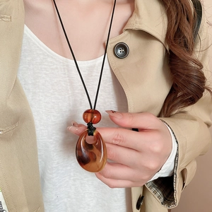 Model wearing retro amber acrylic drop pendant on a black cord necklace with khaki coat