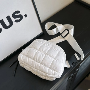 Detail view of white quilted fanny pack with wide shoulder strap on black furniture