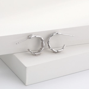 Detail view of silver braided twist hoop earrings on white minimalist display stand