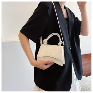 Detail of creamy white hourglass bag with glitter finish and knotted handle on model
