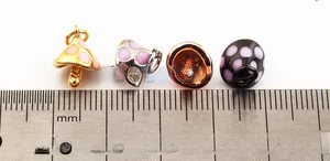Macro shot showing 10mm mini mushroom charms with colorful enamel dots on a white base