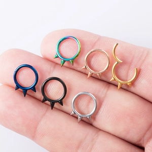 Three-spike circular nose rings and earrings set in six metallic colors on a fingertip