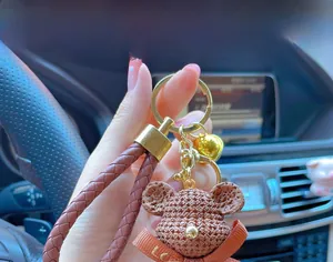 Detailed close-up of a brown resin bear keychain with woven strap and a golden bell