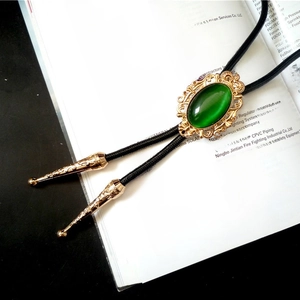 Detail of vintage gold crown bolo tie with green stone on antique book pages